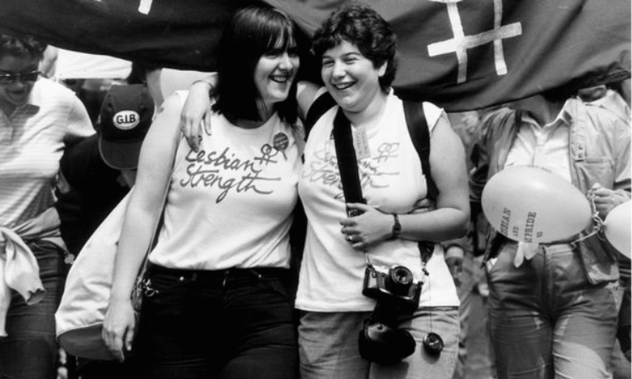 Black and white photo of two women at a march with their arms around each other smiling