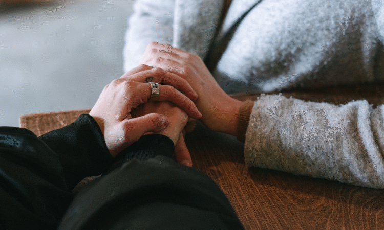 A close up picture of two people holding hands in a supportive way