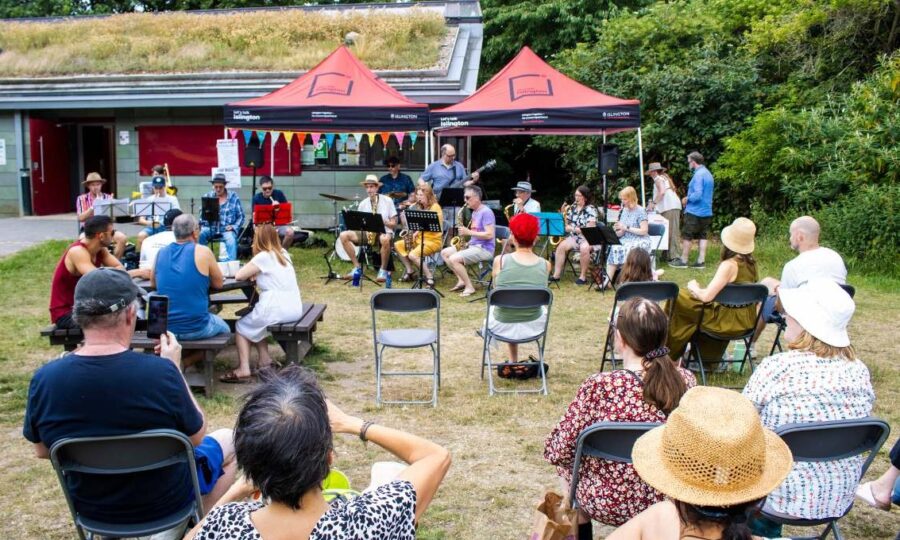 Group of people sat outside in a park on chairs with market stalls around them