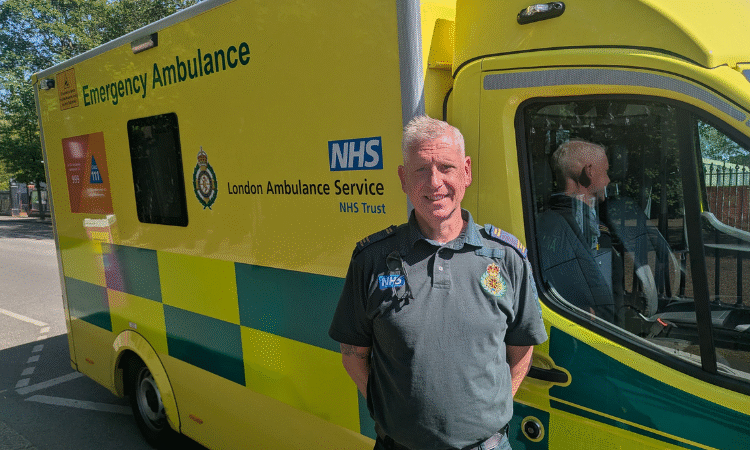 An man who is also an Emergency Medical Technician stood in front of an ambulance on a sunny day